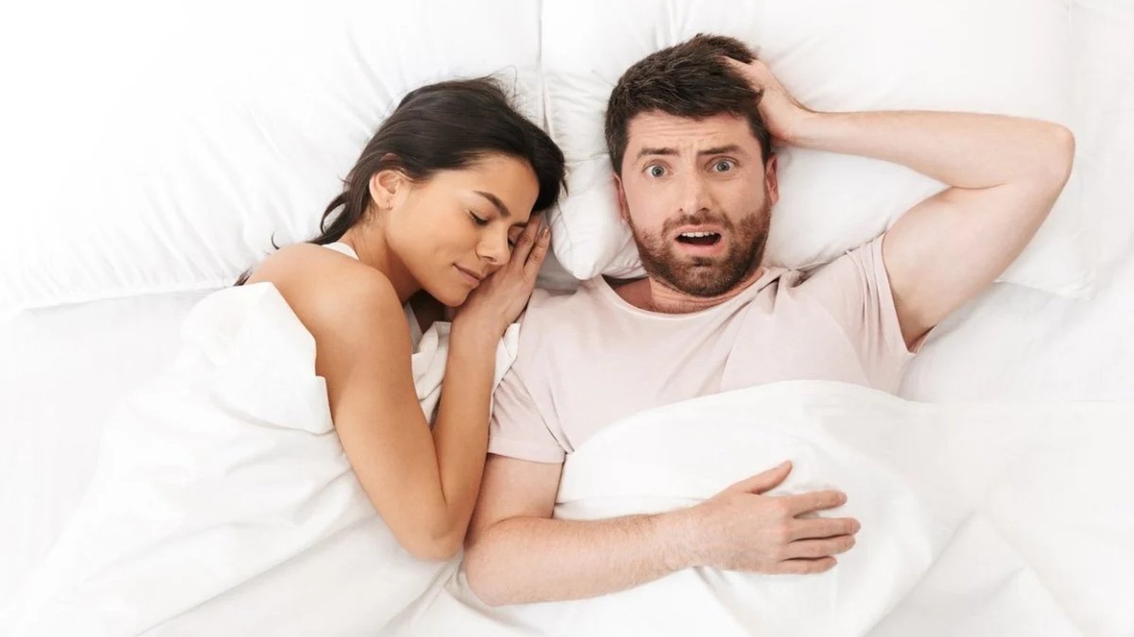 Person lying awake next to a snoring partner in a noisy bedroom