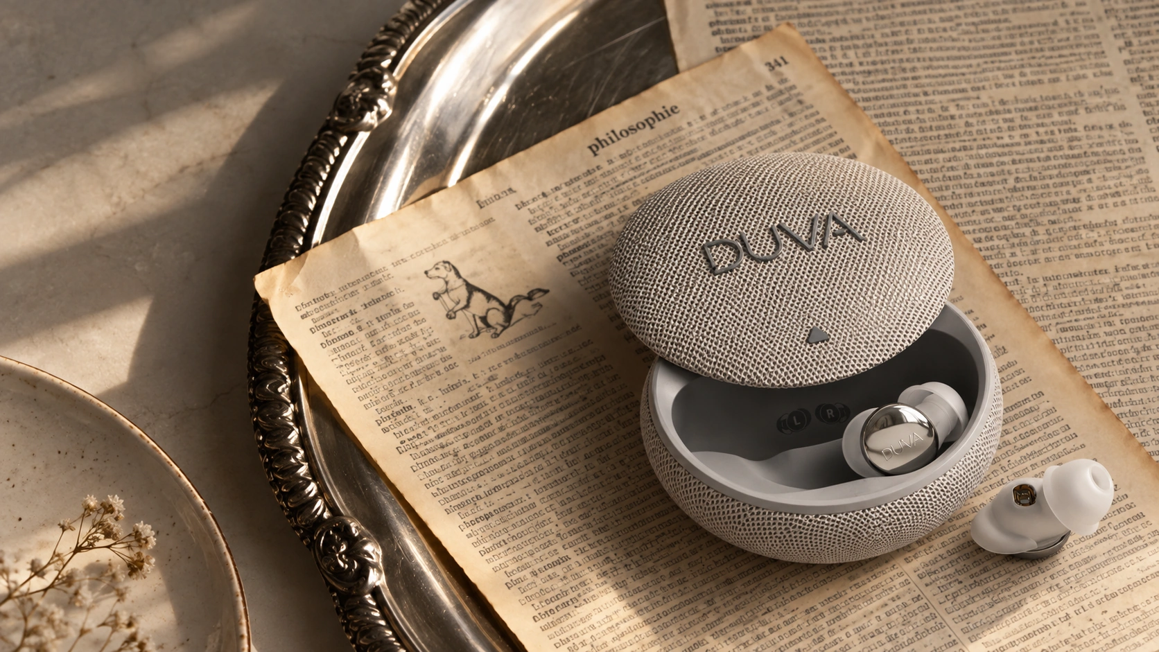 DUVA earbuds and an open charging case on newspaper in a metal tray.